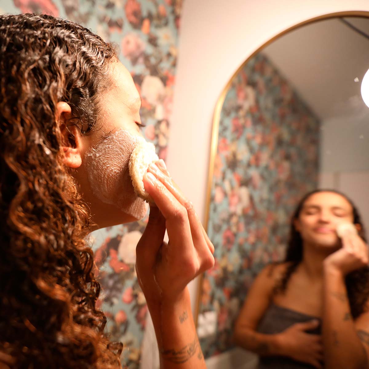 Noia mirant-se al mirant-se al mirall i rentant-se la cara amb una esponja.